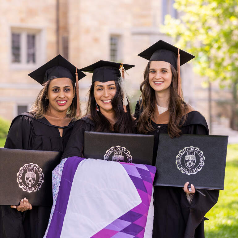 group of three woman in graduation robes with diploma
